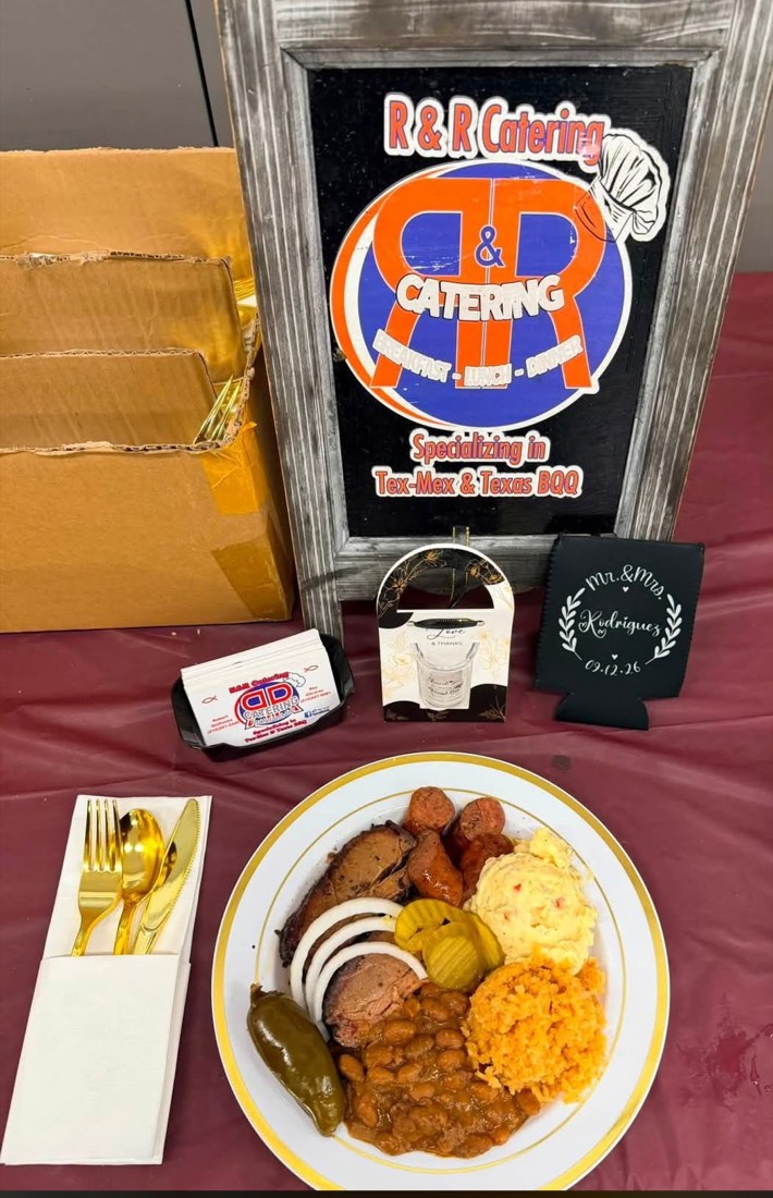 Barbecue plate with smoked meat, beans, Spanish rice, potato salad, bread, pickles, and onions beside an R&R display