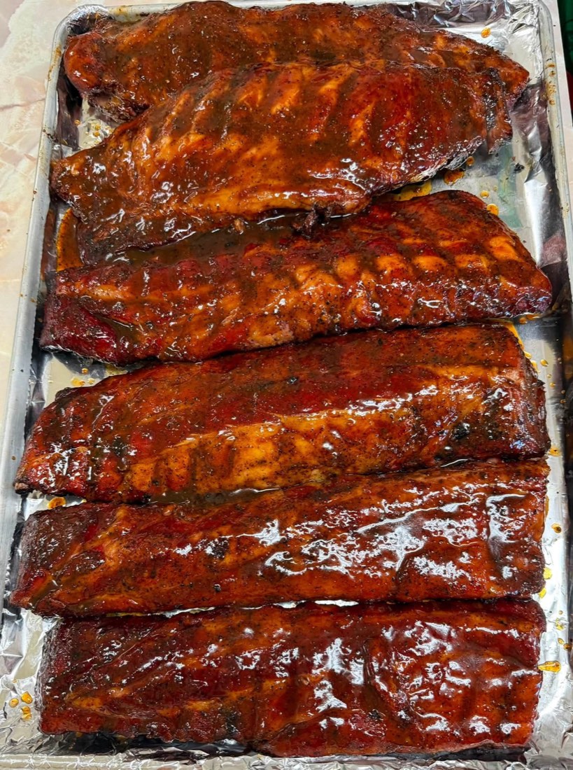 Catering tray filled with sliced brisket, sausage, ribs, and smoked chicken