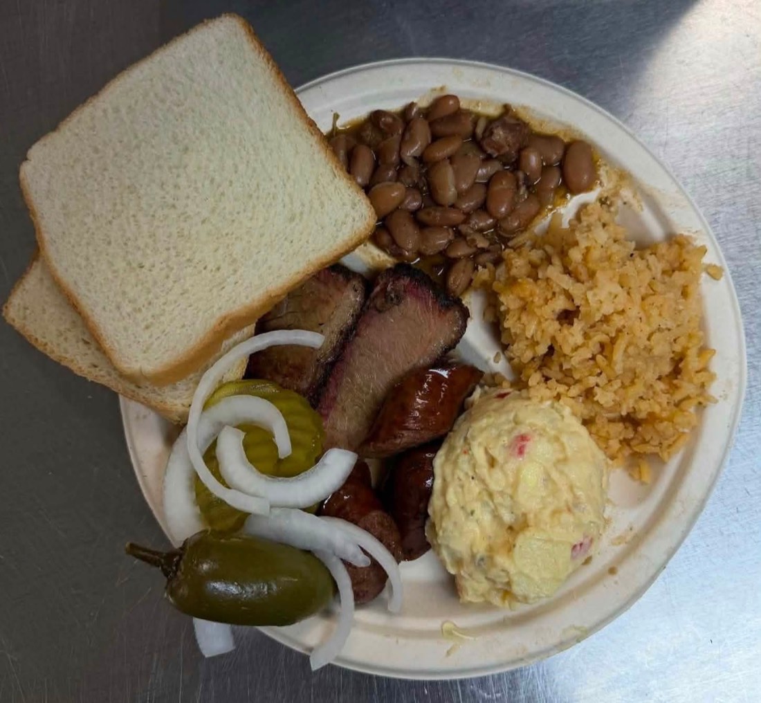 Catering tray piled with dark-barked smoked brisket and ribs
