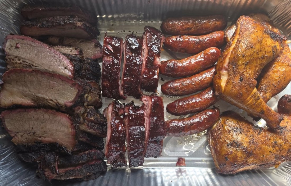 Catering tray of brisket, glazed ribs, sausage, and smoked chicken