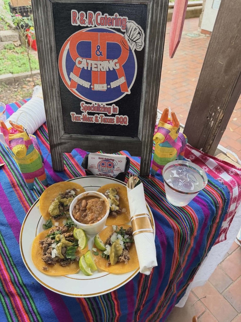 Four tacos topped with onion, cilantro, green salsa, and lime beside beans