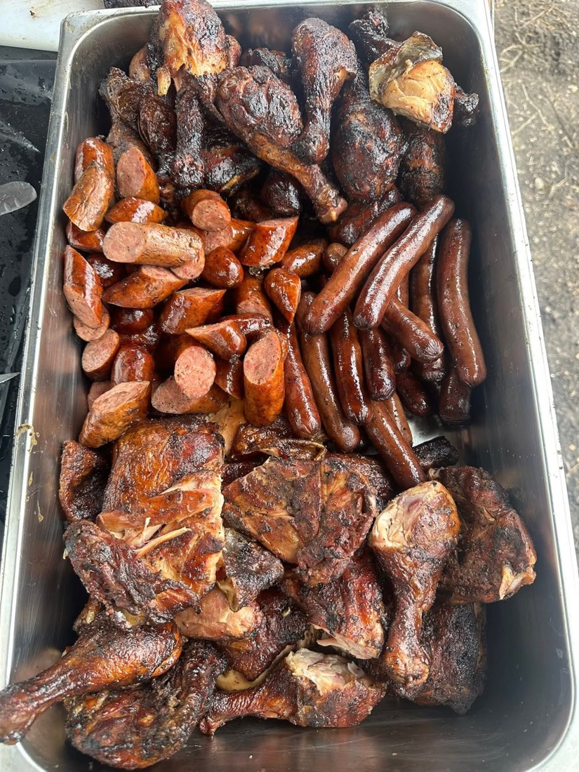 Catering tray of smoked chicken pieces, sliced sausage, and whole sausage links