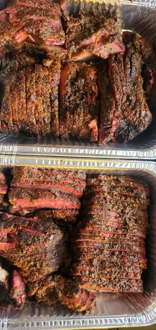 Trays of sliced smoked brisket with a dark seasoned bark