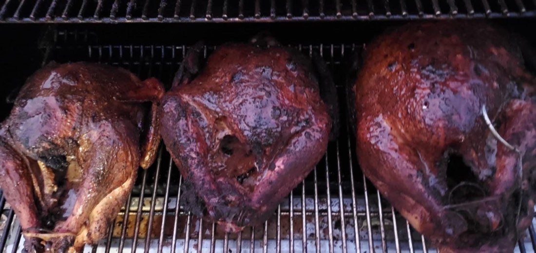 Three whole smoked turkeys resting on a smoker grate