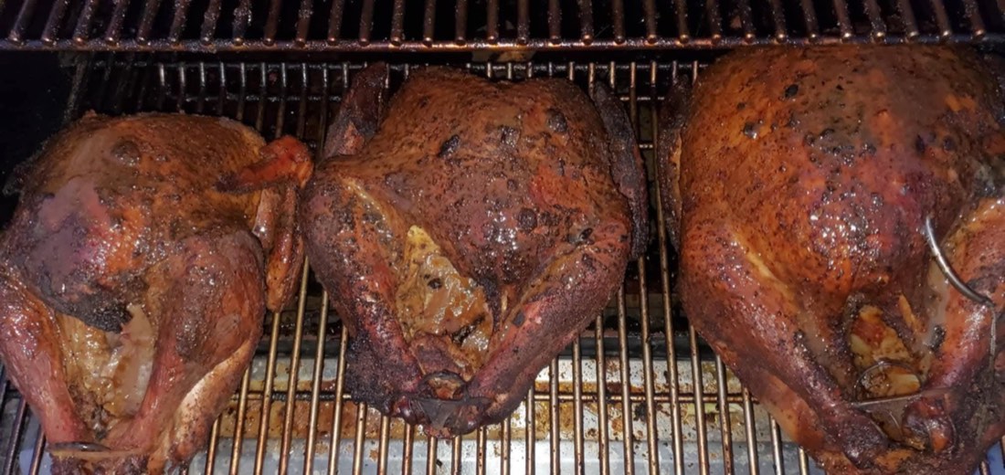 Three glazed smoked turkeys cooking on a smoker