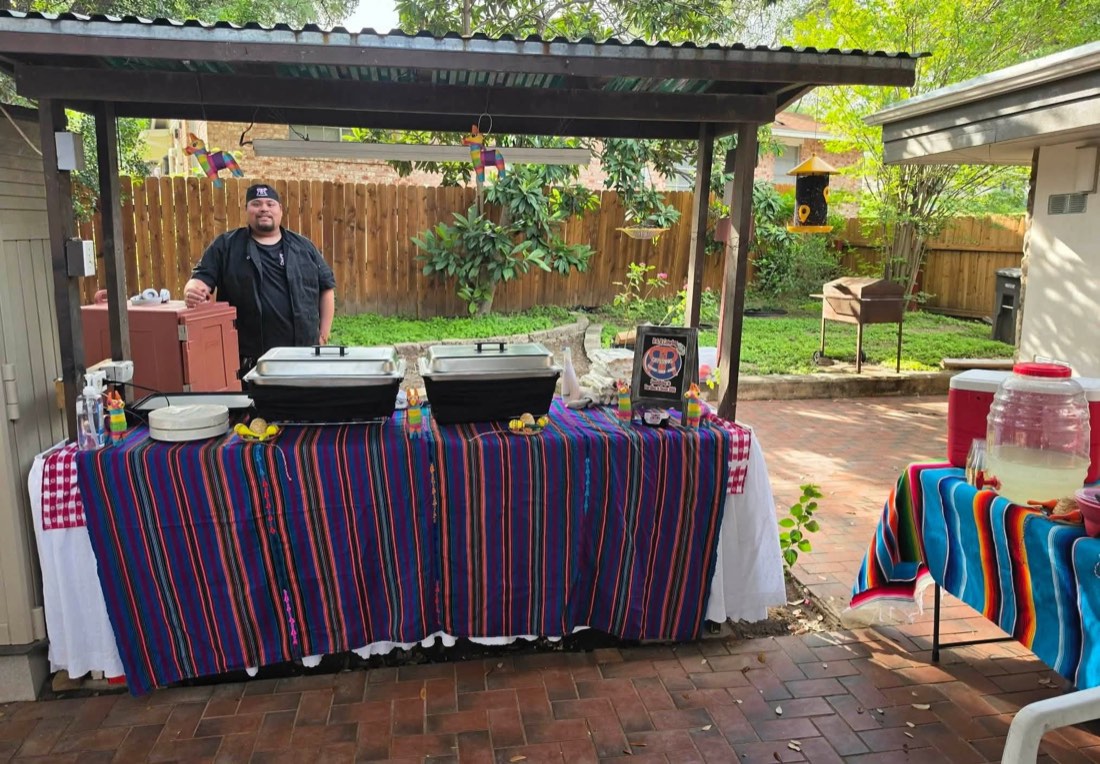 Outdoor R&R Catering station with colorful table coverings, serving pans, and a team member