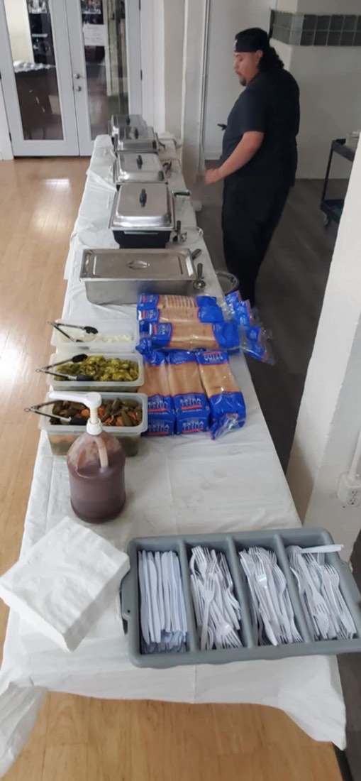 Long indoor buffet line with chafing dishes, condiments, bread, utensils, and a team member