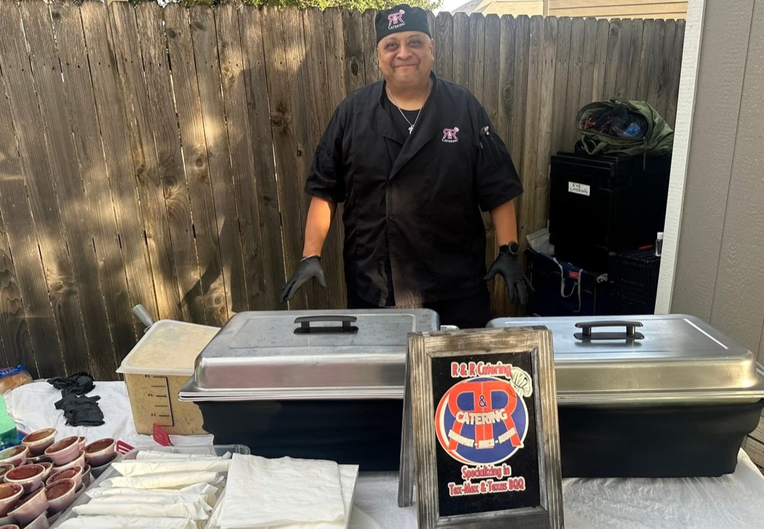 Smiling R&R Catering team member behind an outdoor serving station