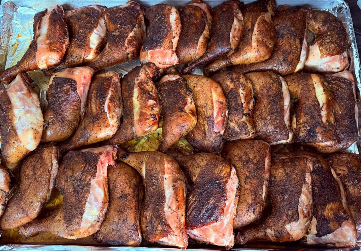 A large catering tray of seasoned smoked chicken leg quarters